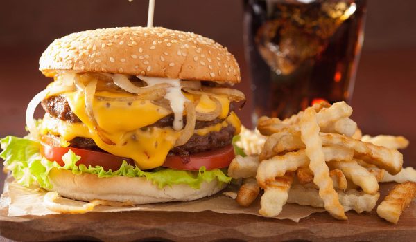 Double cheeseburger garnished with tomato, lettuce, onions, and a side of crinkle cut fries with an iced cola drink